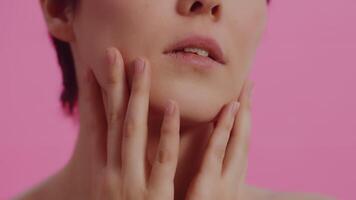 Young beautiful woman with clean skin touching her cheeks with both hands on a pink background close up. Concept of skin care for health and beauty video