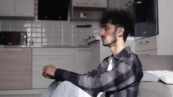 cansado joven hombre sentado en el cocina a hogar y cubierta su cara con su manos después un difícil trabajo día. concepto de cansancio y agotamiento video