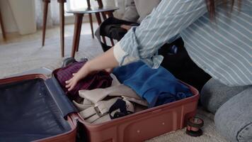 Young man and young woman together folding their clothes into a suitcase, which laying on a floor in a living room, and zipping it up during preparation to the vacation close up video