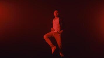 Young asian male performer dance vigorously and passionately in a contemporary style illuminated by red lights on a dark stage, full-length view. Modern show with concert light video