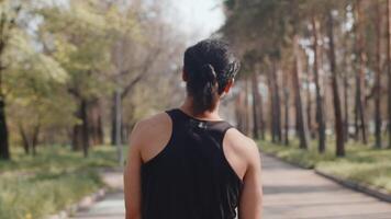 Young asian male athlete in black sportswear walking down the alley in an autumn city park and then start to run, back view. Concept of modern outdoor sports training in a casual urban life video