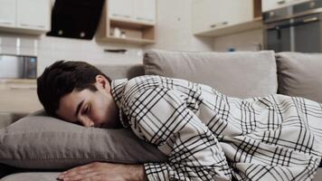 Tired young caucasian man falling face down into a pillow on a couch at home after a hard work day. Concept of excessive fatigue because overtiming video