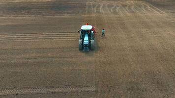 Aerial view of a farmer standing next to a tractor in an open field The tractor preparing the soil for planting, with visible tire tracks on the ground The expansive farmland highlights video