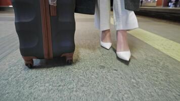 A traveler pulls a black suitcase on wheels while walking in an airport terminal The image captures the lower half of the person, showcasing their stylish white shoes and part of their outfit video