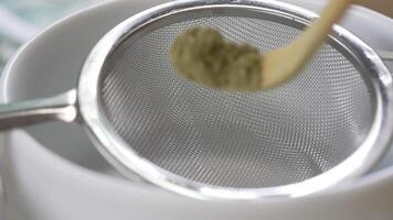 cerca arriba y lento movimiento imágenes de pequeño cuchara cucharón matcha polvo a tamizar en multa té tamiz. verde té ceremonia concepto video