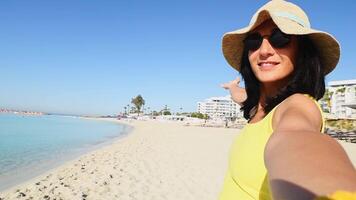 Young joyful caucasian woman in yellow shirt wear hat smiling at camera on the beach - Traveler girl enjoying freedom taking selfie - Well being, healthy lifestyle and happy people video