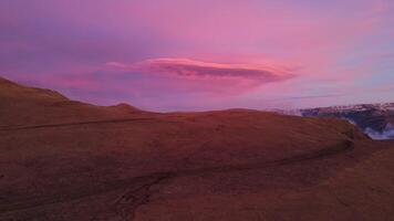 uma magenta nuvem paira dentro a céu Como a Sol conjuntos sobre a montanha declive video