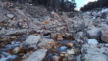 água fluxos através rochoso terreno, cercado de árvores dentro uma natural panorama video