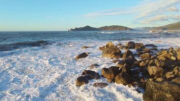 água ondas batida em pedras às natural panorama costa, debaixo nublado céu video