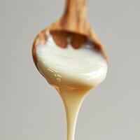 Close-up image of a wooden spoon covered in thick, white condensed milk against a pale grey background. photo