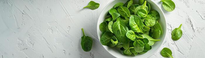 Fresh green spinach leaves in a white bowl on a white concrete background. Top view, copy space. photo