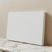 A blank canvas sits on a marble table against a beige wall. photo