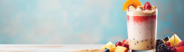 A tall glass of fruit smoothie on a table with fruit scattered on the table next to it. photo