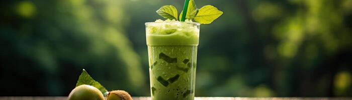 A glass of green smoothie on a wooden table with a blurred background of green leaves. photo