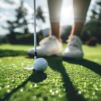 A close up of a golf ball on the green with a club and the golfers feet in the background. photo