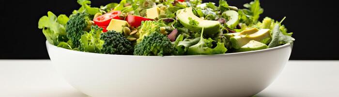 A large white bowl filled with a fresh green salad with cherry tomatoes, avocado, broccoli, and pumpkin seeds. photo