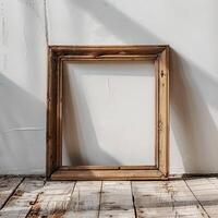 An empty wooden frame is placed on a wooden floor against a white concrete wall with shadows photo