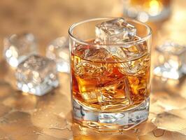 A glass of amber liquid, likely whiskey, with ice cubes in it, sitting on a reflective surface, perhaps a bar. photo