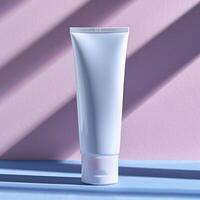 A white plastic tube of face cream on a blue table against a pink background with shadows. photo