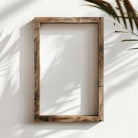 The wooden frame is placed against a white wall, and a palm leaf is placed beside it. The shadows of the palm leaves are cast on the wall and the frame. photo