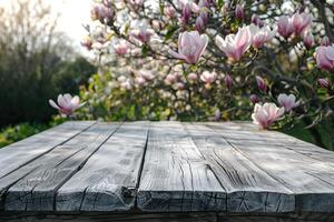 A wooden table in a lush garden with magnolia flowers in the background. photo
