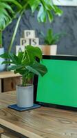 tablet with a green screen propped up against a visually pleasing pot plant sitting on a wooden modern table photo