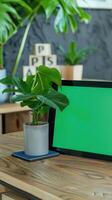 tablet with a green screen propped up against a visually pleasing pot plant sitting on a wooden modern table photo