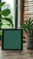 tablet with a green screen propped up against a visually pleasing pot plant sitting on a wooden modern table photo