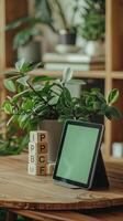 tablet with a green screen propped up against a visually pleasing pot plant sitting on a wooden modern table photo