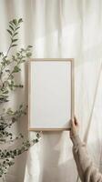 A mockup of a minimalistic A4 frame A woman's hand holding the wooden A4 frame visible danish pastel aesthetic in the room photo