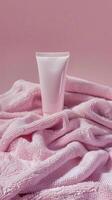 a tube of body cream sitting inside of a pink towel photo