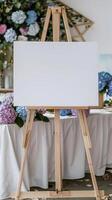 A white blank horizontal poster on easel in front of wedding reception tables with pastel blue and purple colors hydrangea flowers photo