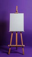 An easel with a white canvas on a stretcher stands in a clean purple blue room photo