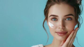 A beautiful young woman with perfect skin applying skincare cream Set against a pale blue background photo