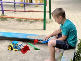 A little boy playing in the sandbox at the playground outdoors. Child playing with sand cars. Outdoor creative activities for kids. photo