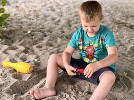 niño jugando en salvadera. pequeño chico teniendo divertido en patio de recreo en mina de arena. verano y infancia concepto. foto