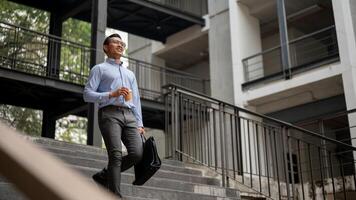 A confident businessman walks down stairs outside a building, holding a coffee cup and a briefcase. photo