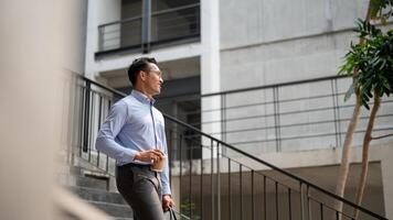 A confident Asian businessman walking down the stairs, holding a coffee cup and a briefcase. photo