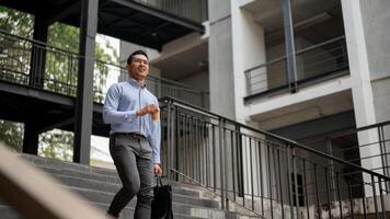 A confident businessman walks down stairs outside a building, holding a coffee cup and a briefcase. photo