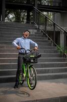 An exuberant Asian millennial businessman joyfully rides a green bicycle down stairs. photo