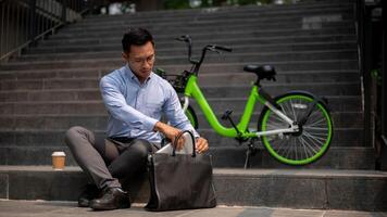 un determinado asiático empresario se sienta en pasos al aire libre, organizando su ordenador portátil en su maletín bolsa. foto