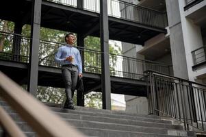 A confident businessman walks down stairs outside a building, holding a coffee cup and a briefcase. photo