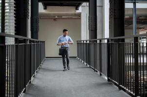 A confident Asian businessman is checking time on his wristwatch while walking along a corridor. photo
