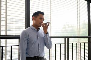 A determined businessman sending his voice message via his smartphone while standing in a corridor. photo