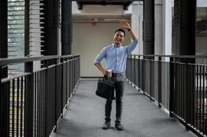 A friendly Asian businessman waving to greet his colleague while walking along the building corridor photo
