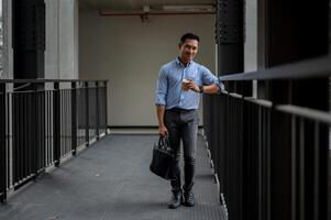 A handsome Asian businessman standing in the building corridor, taking a coffee break outdoors. photo