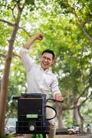 An excited Asian businessman rides a bike triumphantly, raising his fist in celebration. photo