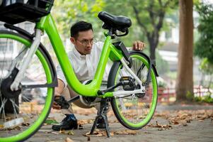 un enfocado empresario inspecciona su bicicleta neumático en un parque, encuentro un problema durante su desplazarse. foto