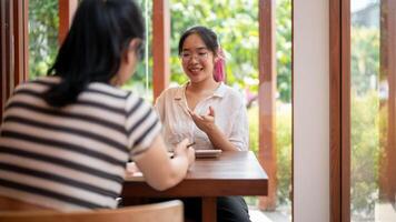 un positivo asiático mujer es teniendo un informal reunión con su cliente a un café tienda. foto