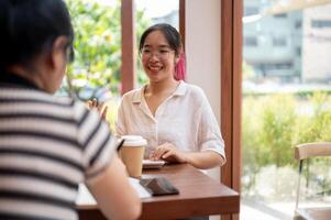 un positivo asiático mujer es teniendo un informal reunión con su cliente a un café tienda. foto